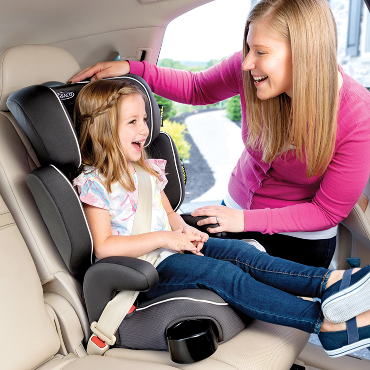 Madre sonriendo y ajustando el reposacabezas de su hija sentada en la silla de coche Graco Assure