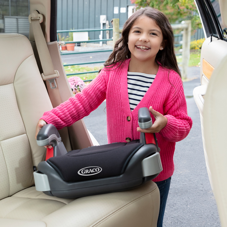 Petite fille plaçant le siège auto Graco Booster Basic dans la voiture
