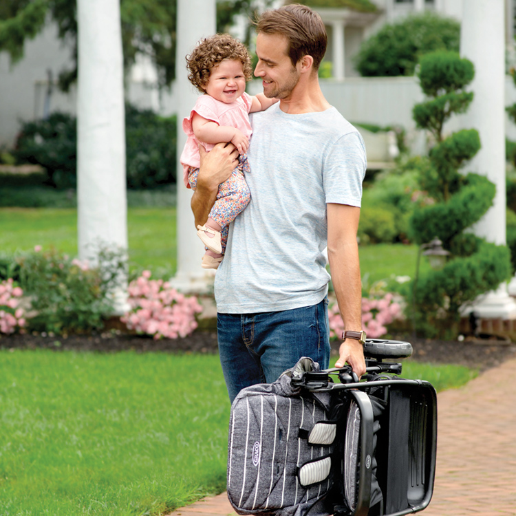 Dad carrying Graco Breaze Lite 2 with one hand while holding his baby in the other