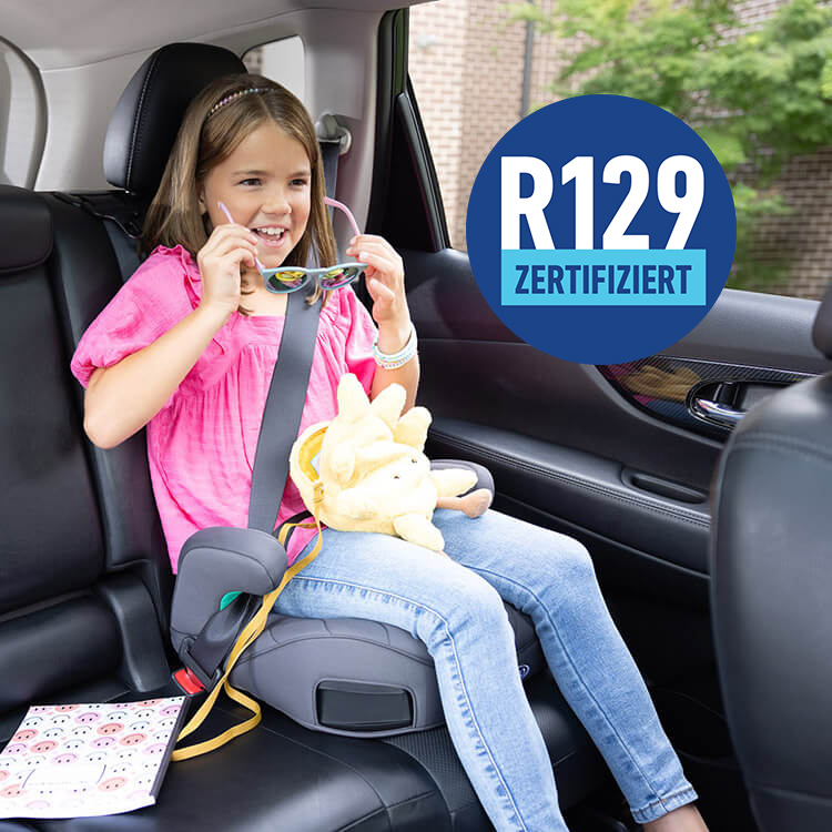 Kleines Mädchen sitzt lächelnd auf der Graco® Booster Max R129 Kindersitzerhöhung mit ISOFIX und setzt sich eine Sonnenbrille auf, auf dem Bild ist ein 