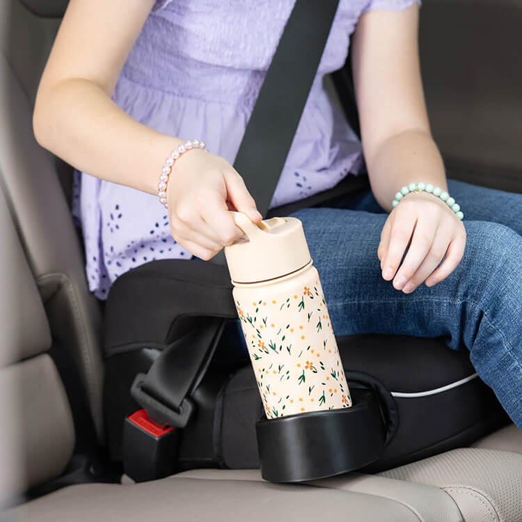 Young girl placing a water bottle in the cupholder of Graco Booster Deluxe R129 backless booster car seat. 
