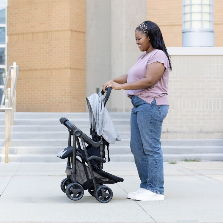 Image of a woman folding Graco DuoRider double pushchair outside in front of a building
