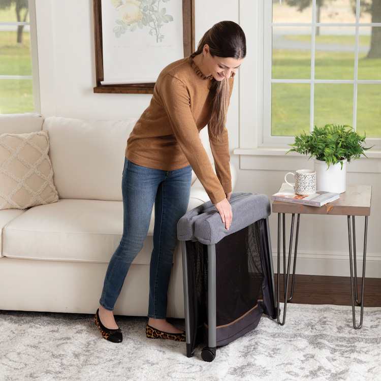 Mum folding Gray Graco FoldLite™ LX Lightweight Travel Cot in living room