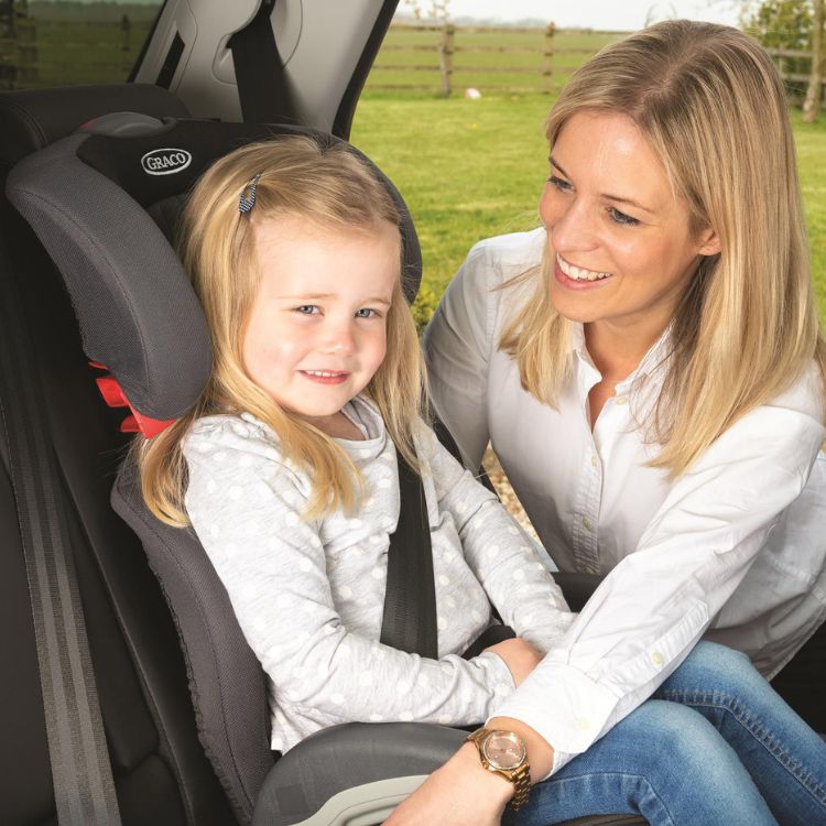 Little girl sitting in Graco Junior Maxi R44 highback booster as her mum helps buckle her up