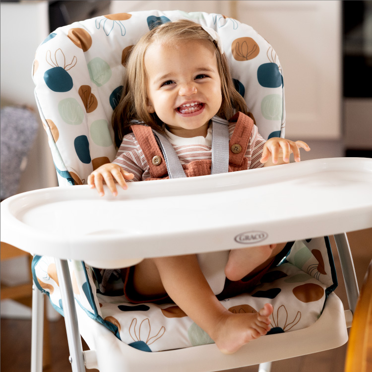 Bambina seduta e sorridente nel seggiolone Graco SnackEase con le mani sul vassoio rimovibile
