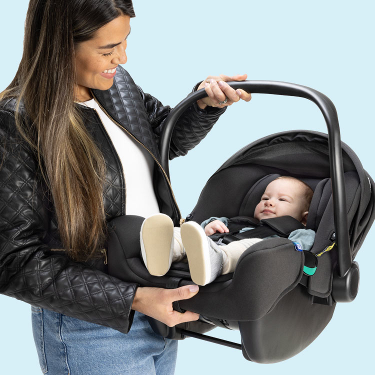 Mom smiling and holding baby that’s sitting in the Graco SnugLite i-Size R129 infant car seat.