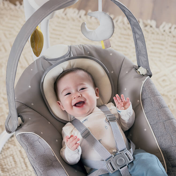 Bébé joyeux installé dans la balancelle intelligente 2-en-1 silencieuse Graco SoftSway au salon. 
