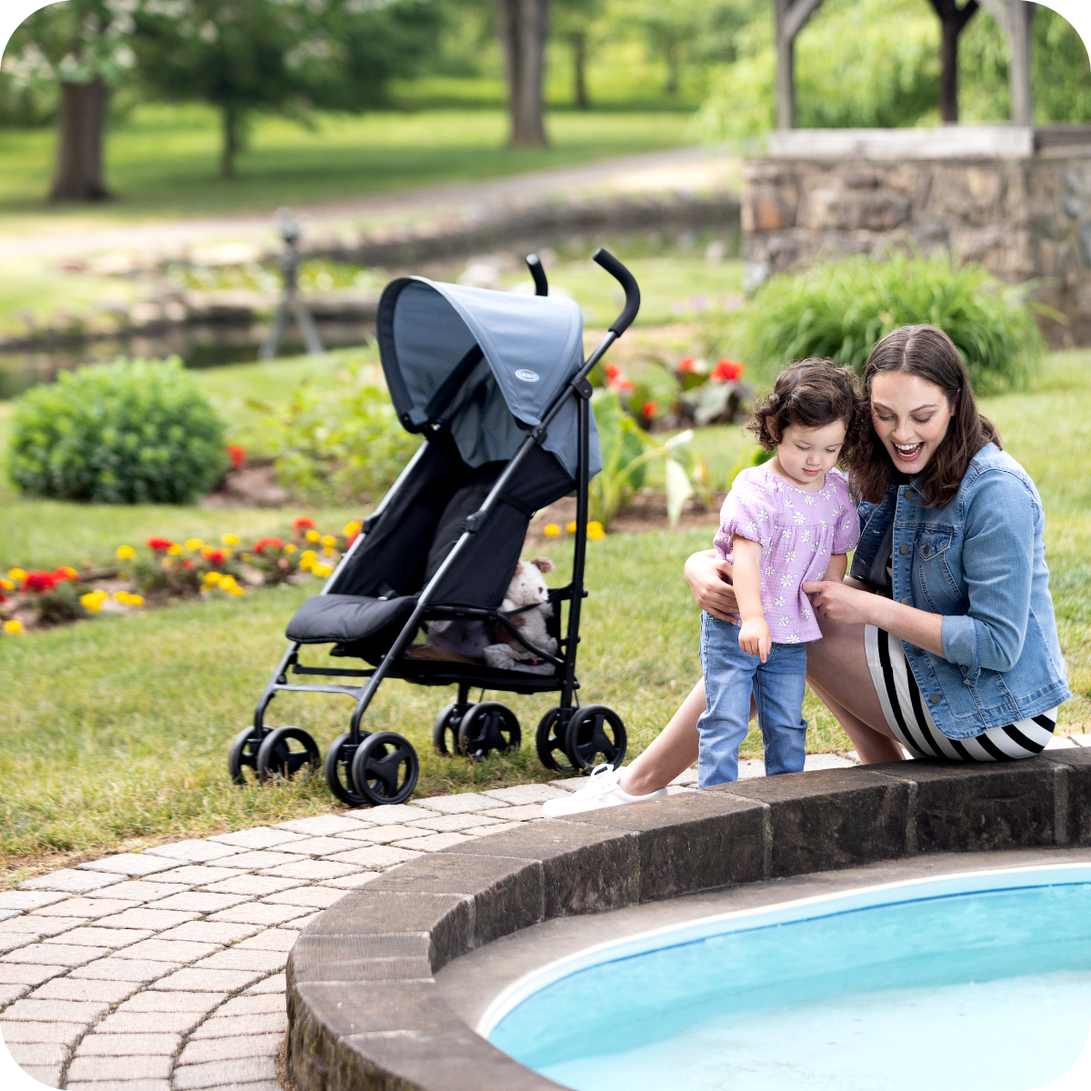Mum and little girl playing at a fountain with Graco EZLite at three quarter angle in the background