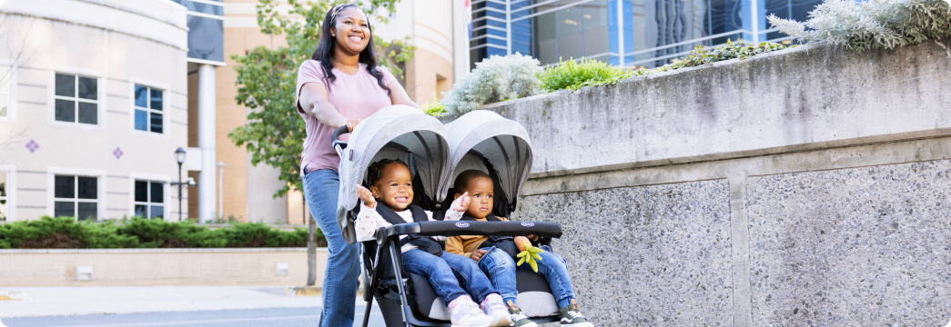 Mum smiling and pushing twins in DuoRider lightweight double pushchair.