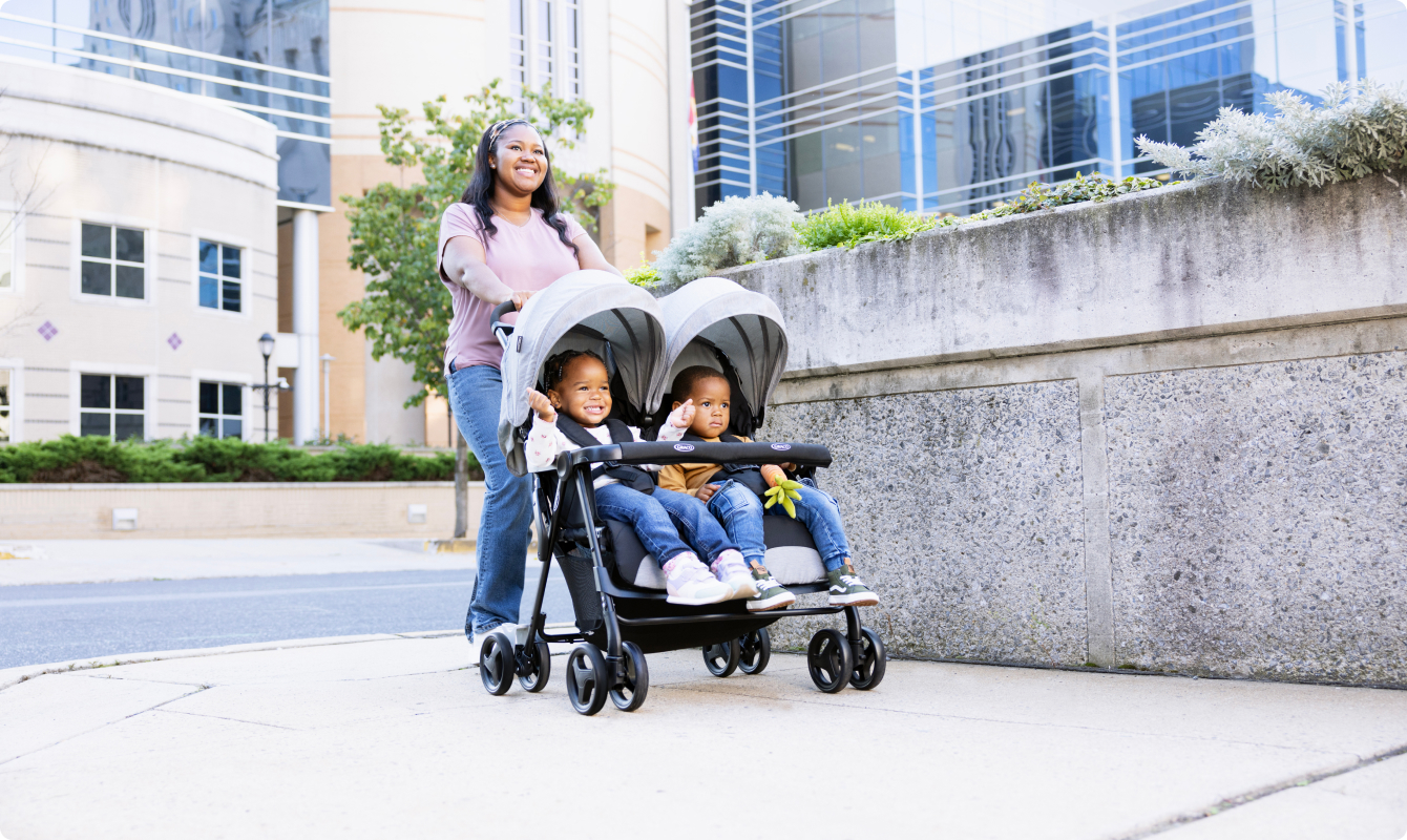 Mum smiling and pushing twins in DuoRider lightweight double pushchair.