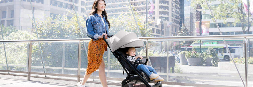 Mamma che sorride e cammina mentre spinge il bambino nel passeggino da viaggio leggero con chiusura compatta Myavo. Mamma sorridente che cammina mentre interagisce con il bambino nel passeggino Near2Me DLX Trio in modalità navicella.