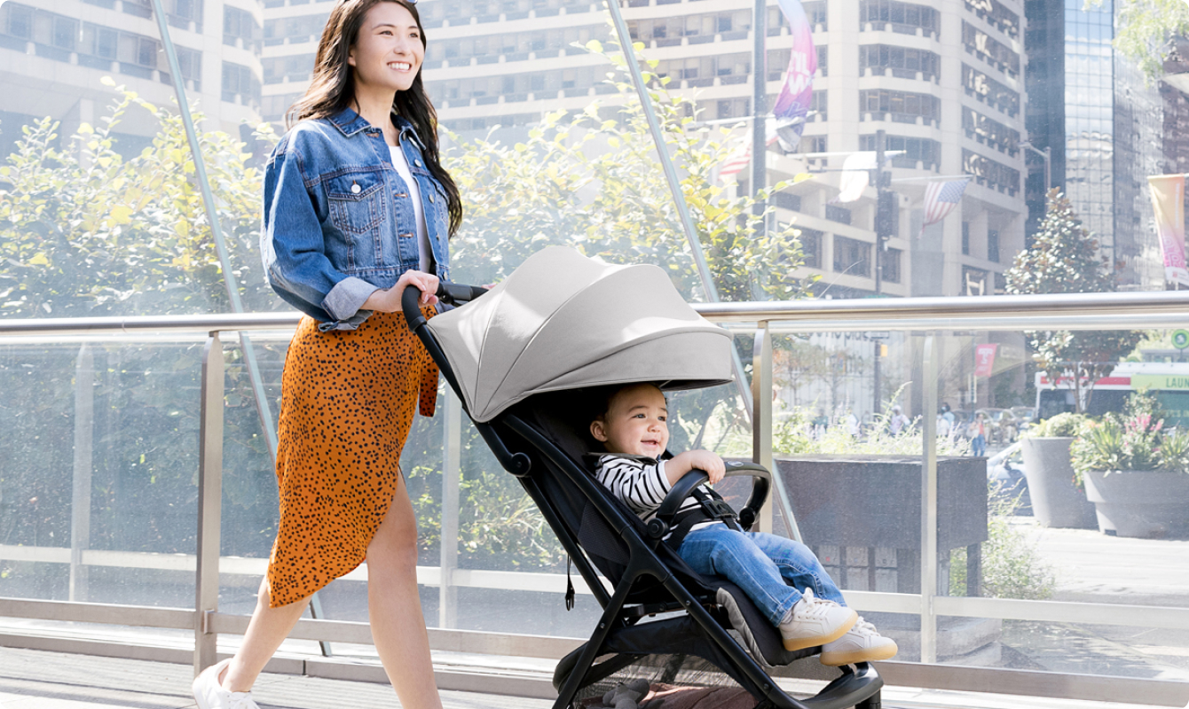 Mamma che sorride e cammina mentre spinge il bambino nel passeggino da viaggio leggero con chiusura compatta Myavo. Mamma sorridente che cammina mentre interagisce con il bambino nel passeggino Near2Me DLX Trio in modalità navicella.