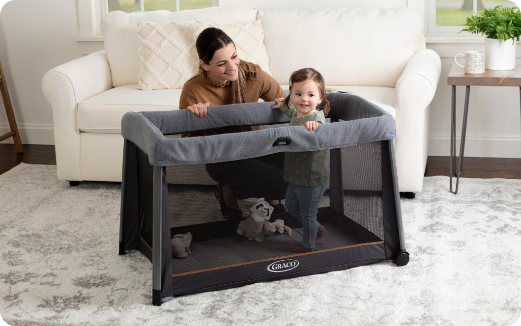 A mum watching a toddler standing in the Graco FoldLite travel cot