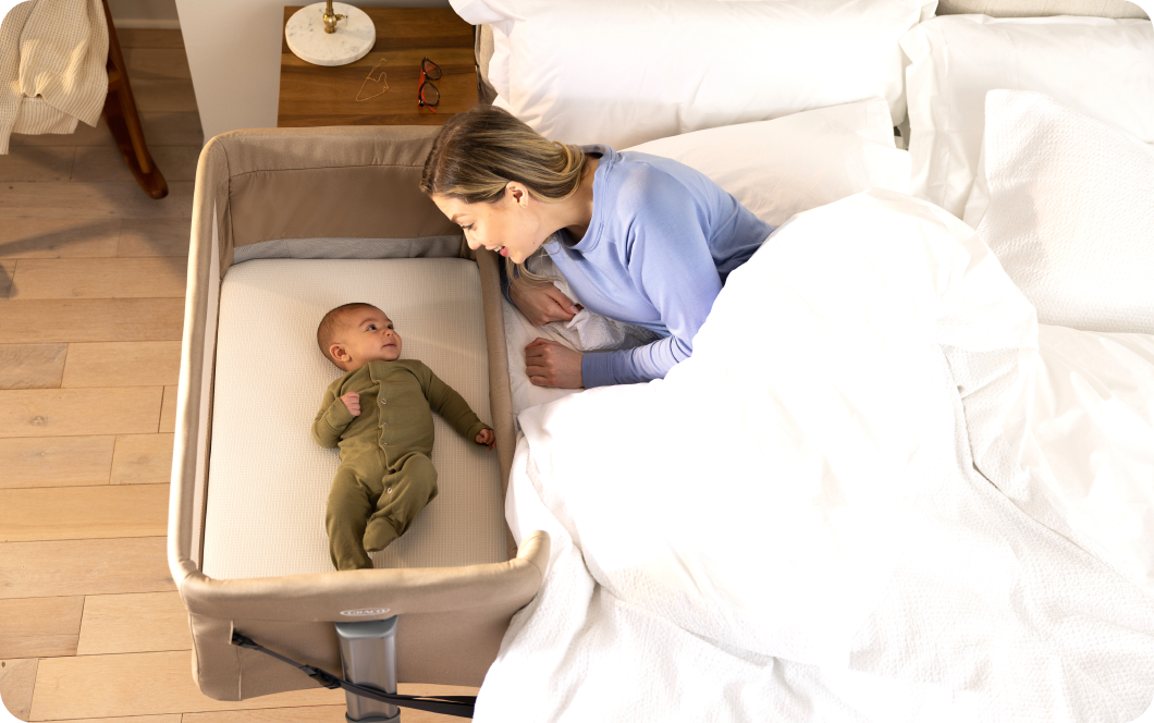 A mother checking on her baby lying in the Graco Sweet2Sleep crib next to her bed